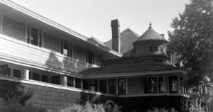 Black and white photograph of the Frank Lloyd Wright Studio in Oak Park, featuring its distinctive architectural elements such as long horizontal lines, large windows, and a conical turret with a rounded balcony.