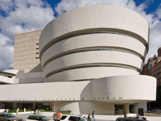 Exterior view of the Solomon R. Guggenheim Museum in New York City, showcasing its distinctive spiral design and modernist architecture with a clear blue sky in the background.