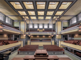 Interior view of Unity Temple showing the sanctuary with its distinctive architectural features. The room is characterized by strong horizontal lines, earthy tones, and geometric shapes.
