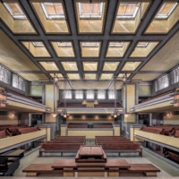 Interior view of Unity Temple showing the sanctuary with its distinctive architectural features. The room is characterized by strong horizontal lines, earthy tones, and geometric shapes.