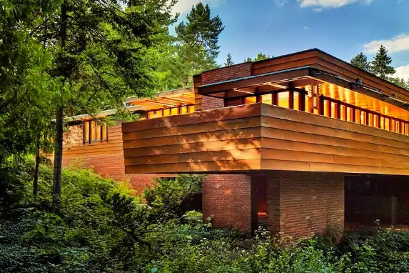 Photograph of a Frank Lloyd Wright-designed residence nestled in a lush forest setting, featuring horizontal lines, large windows, and natural materials that harmonize with the surrounding trees.